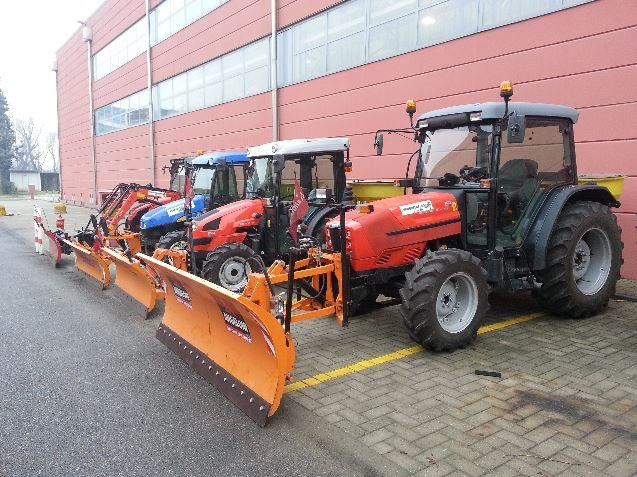 Trattori con lama sgombraneve parcheggiati davanti a un capannone