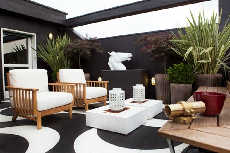 Terrazzo con poltrone in legno, pavimento bianco e nero e piante in vaso